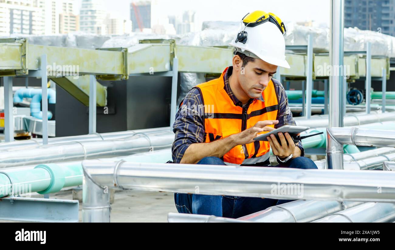 A man in an orange vest sits on pipes, using a smartphone. Stock Photo