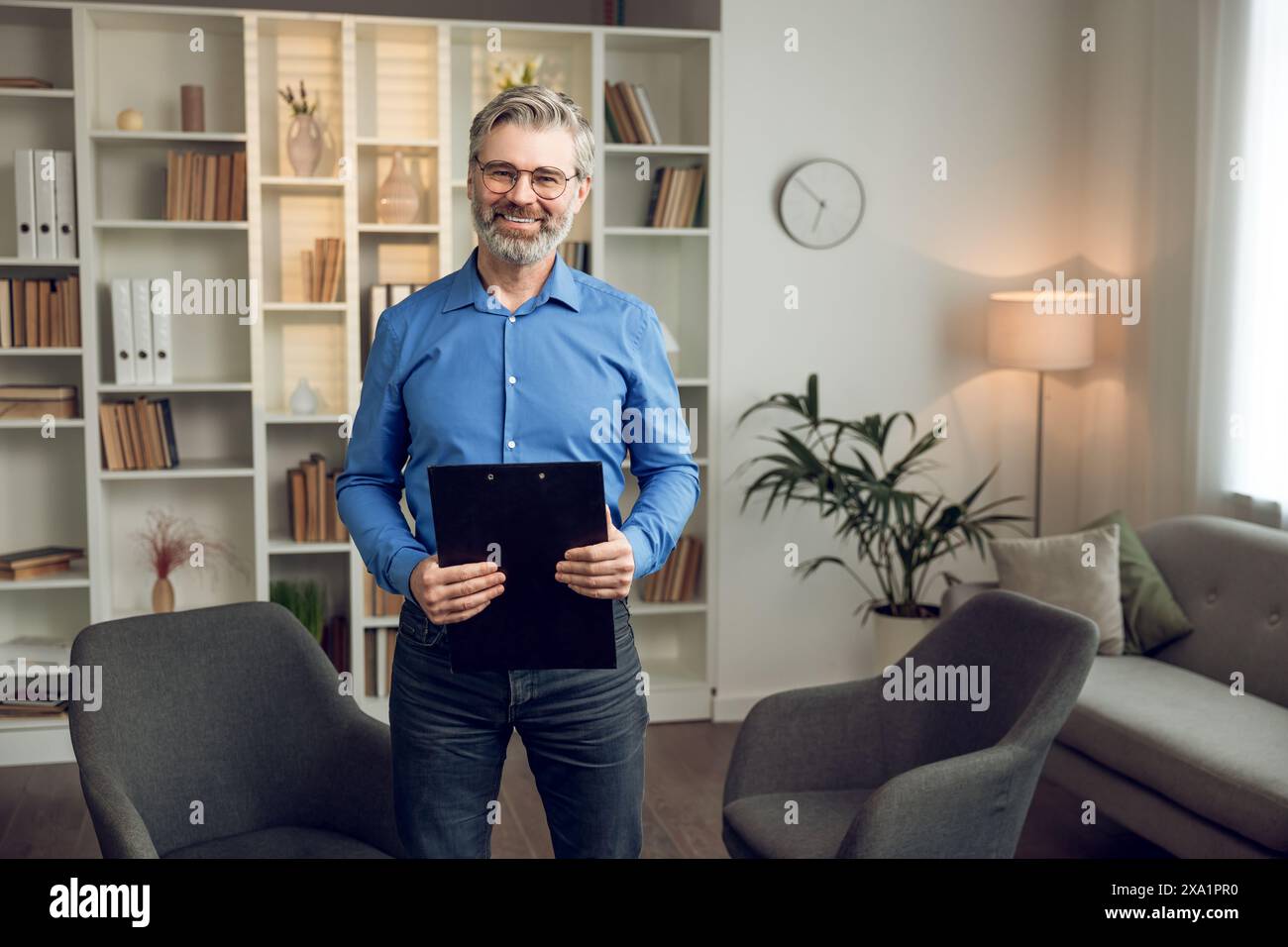 Happy male psychologist with clipboard looking at camera and smiling in modern office Stock Photo