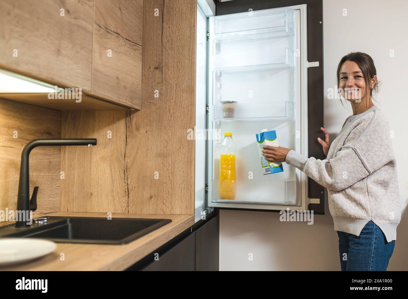 Woman in the kitchen. Young dark-haired woman opening fridge and taking a bottle of milk Stock Photo