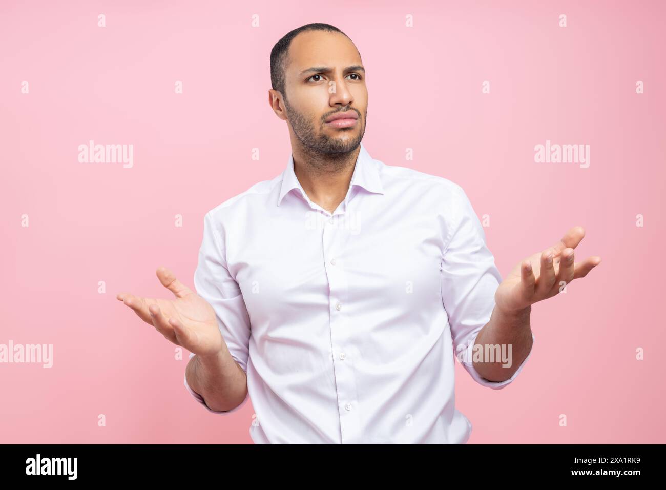 Confused man in white shirt shrugging shoulders isolated over pink background Stock Photo