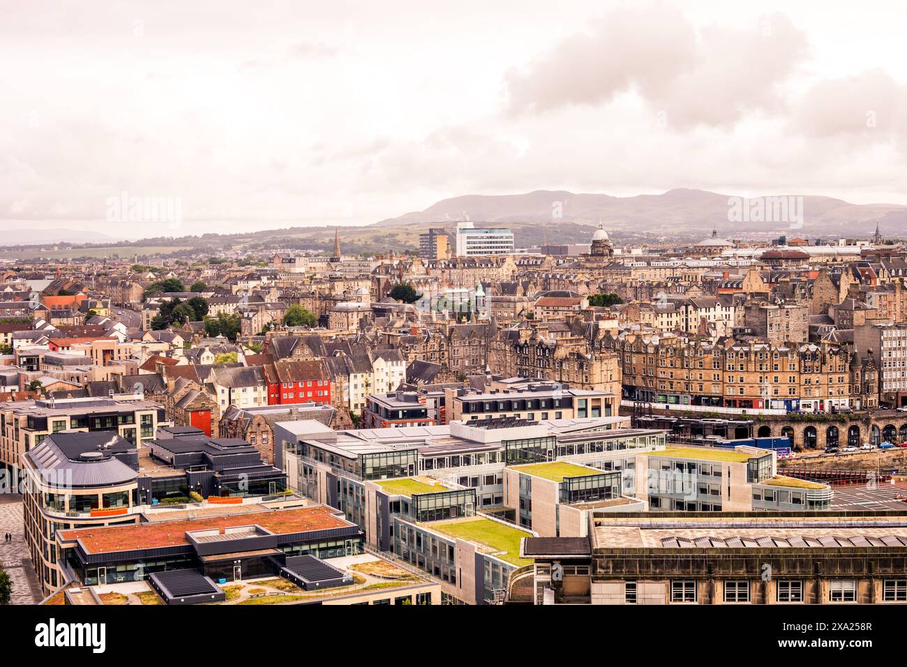 The streets and buildings of Edinburgh stretch out, forming a dynamic tapestry of urban life against the dramatic backdrop of Scotland's mountainous t Stock Photo