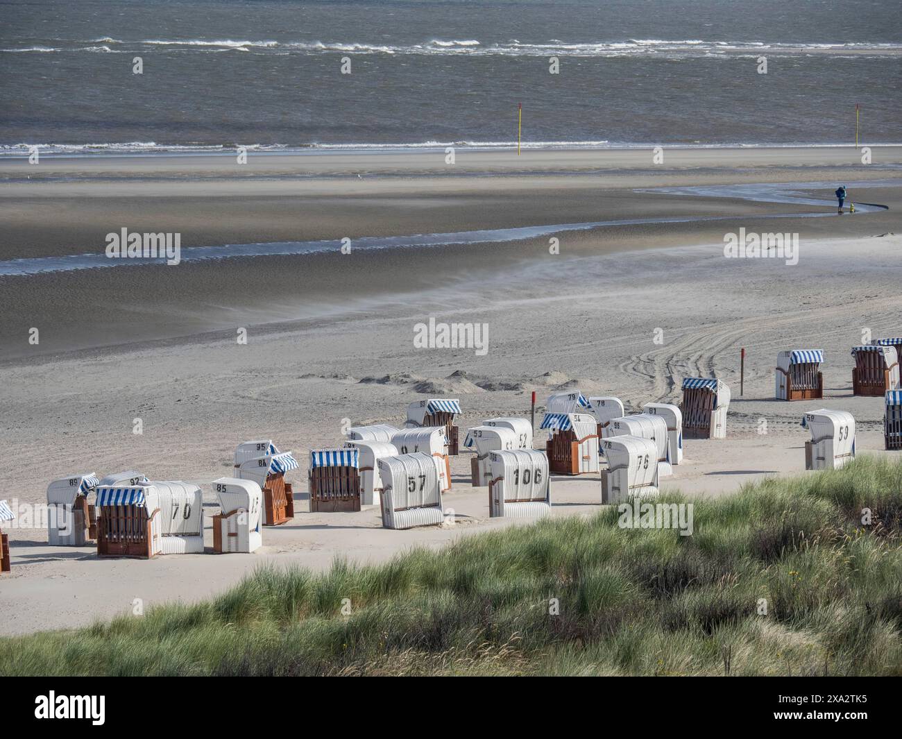 A beach with several beach chairs, in the background the sea and a person. Windy and quiet, Spiekeroog, Germany Stock Photo