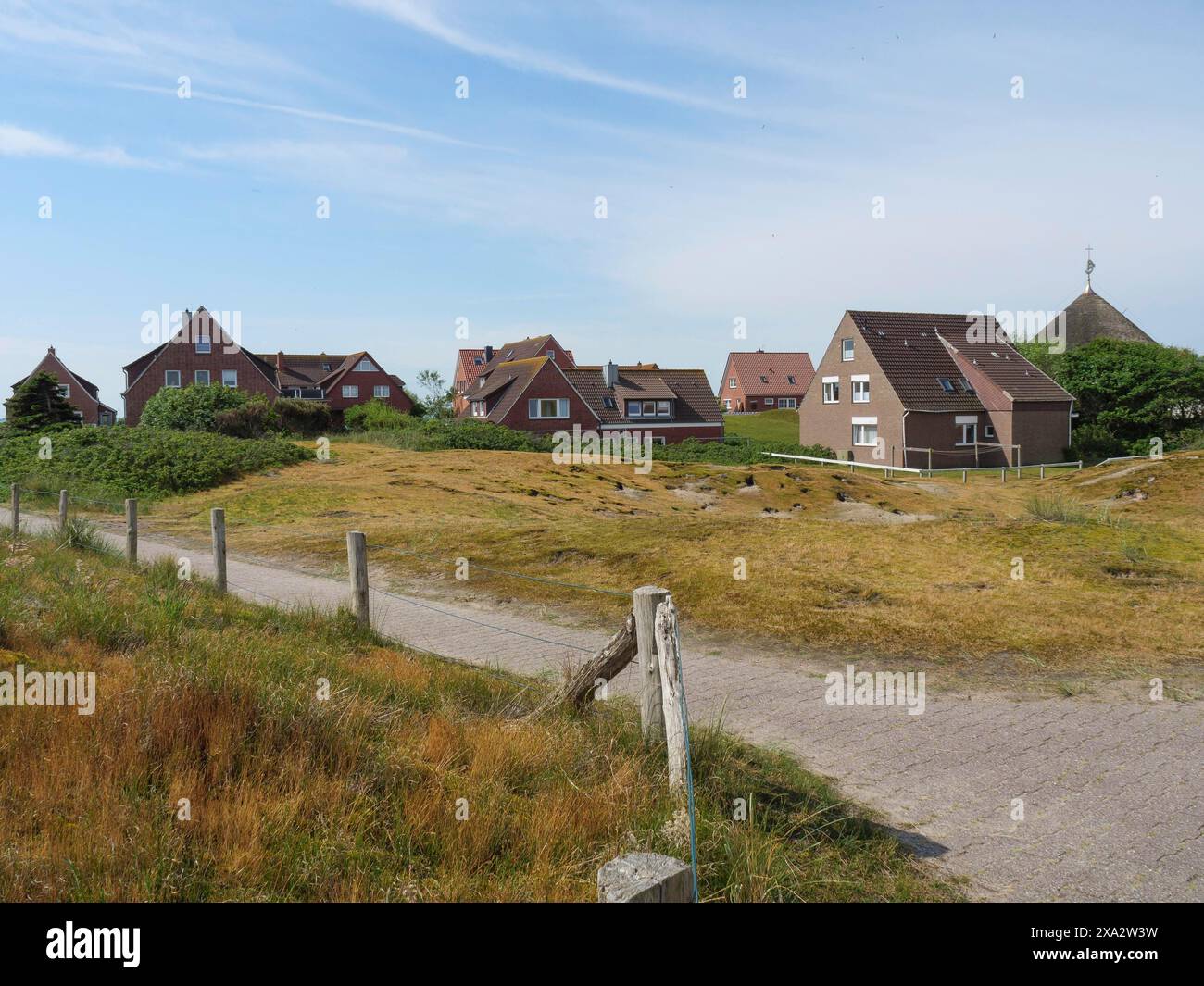 Rural scene with several brick houses in the background and a path through a meadow, Baltrum Germany Stock Photo