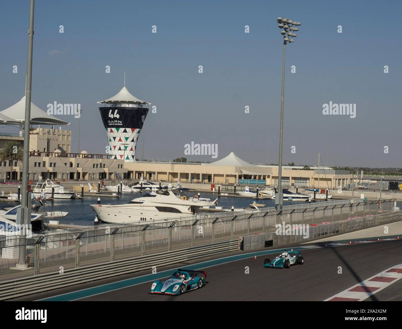 Racing cars drive past a marina, buildings and a striking tower can be ...