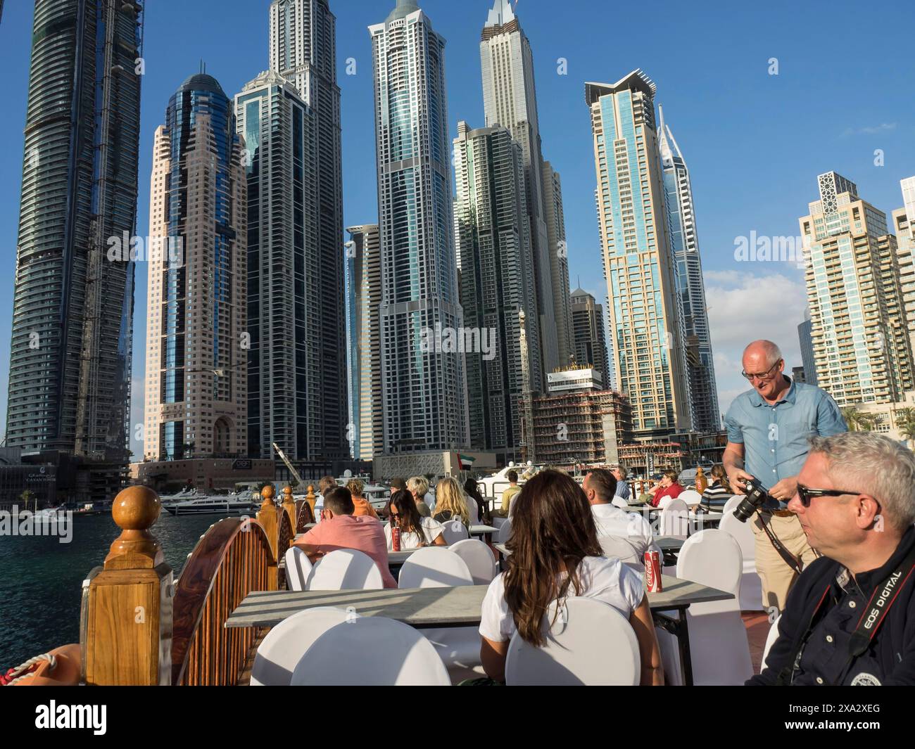 People sitting in an outdoor restaurant by the river with a view of a skyline of modern skyscrapers, dubai, arab emirates Stock Photo