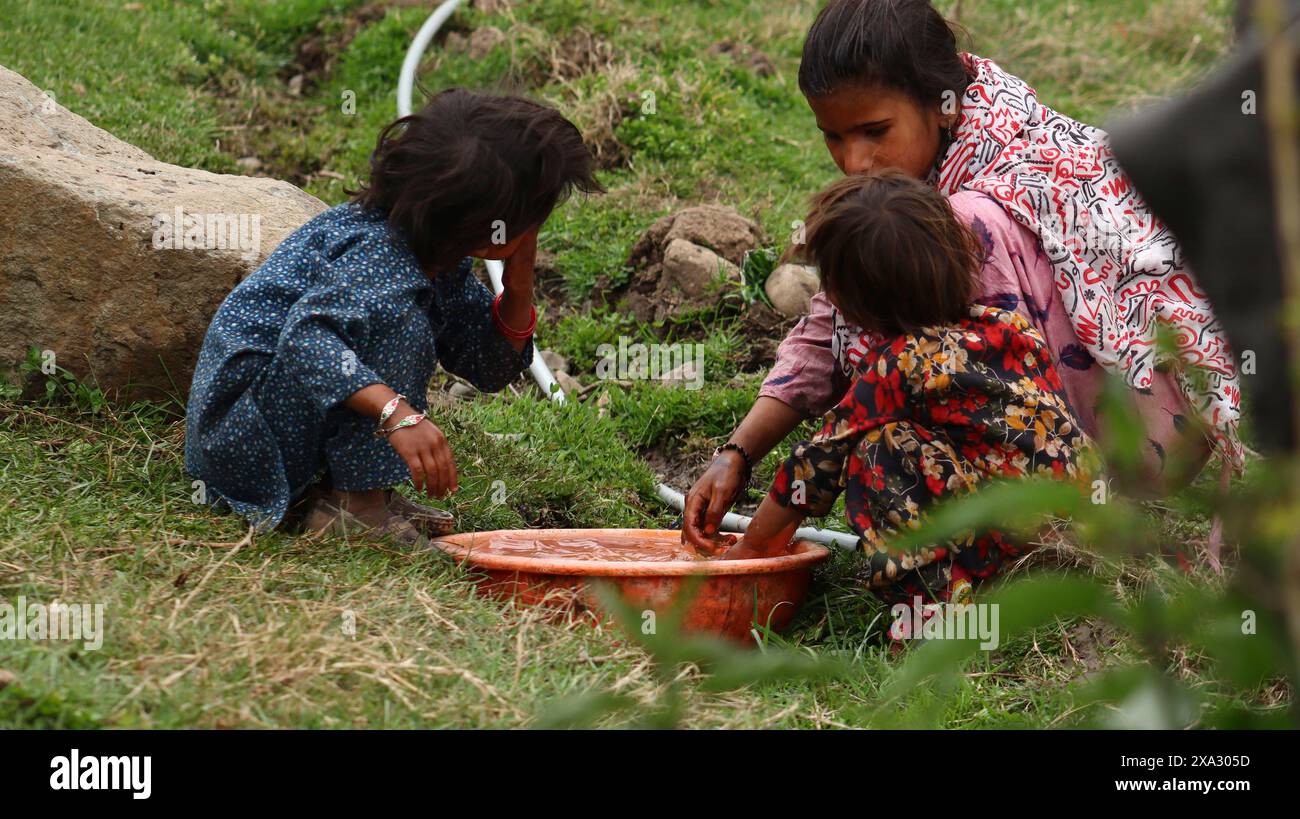 A woman and two children crouching near a wash basin in a rural area, engaged in washing activities, Jammu and Kashmir, India Stock Photo