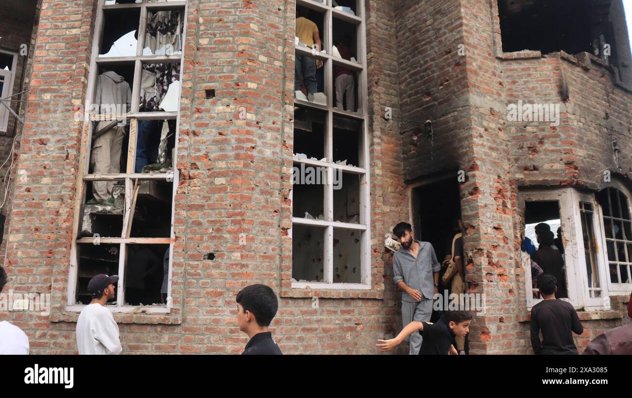 People gather around a multi-story damaged brick building with several broken windows, Encounter, Pulwama, Jammu and Kashmir, India Stock Photo