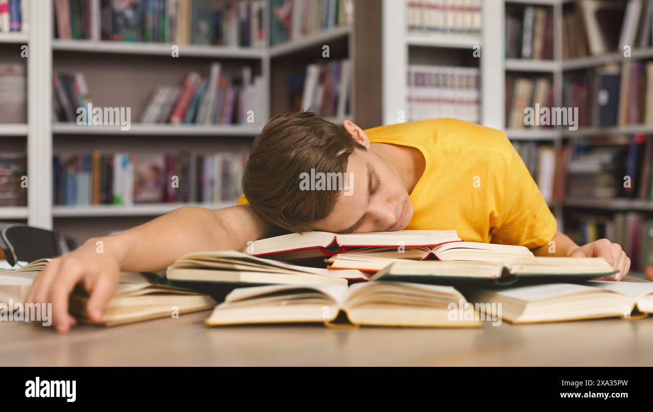 Tired guy napping on books in library Stock Photo