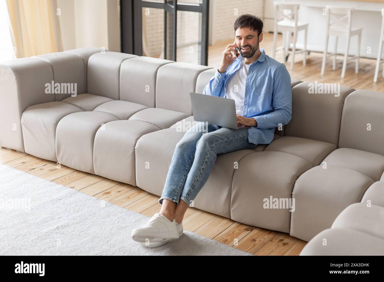 Man Uses Laptop and Cell Phone While Sitting on Sofa Stock Photo