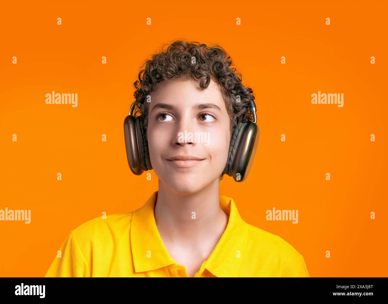 Thoughtful boy with curly hair wearing headphones and a yellow shirt ...