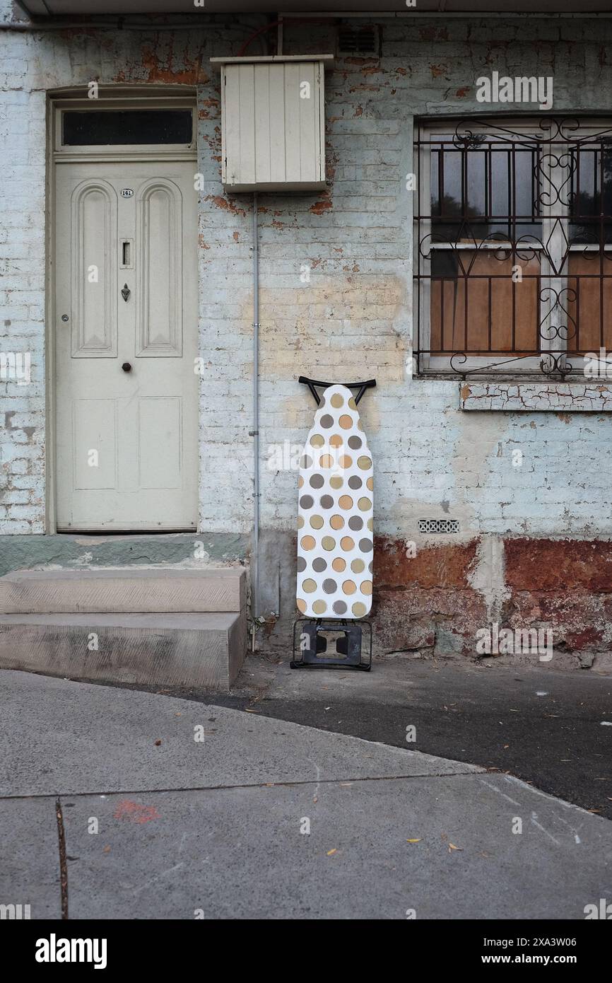 An ironing board with a cover of coloured circles against the weathered front wall of a terrace house in Surry Hills, Sydney Stock Photo