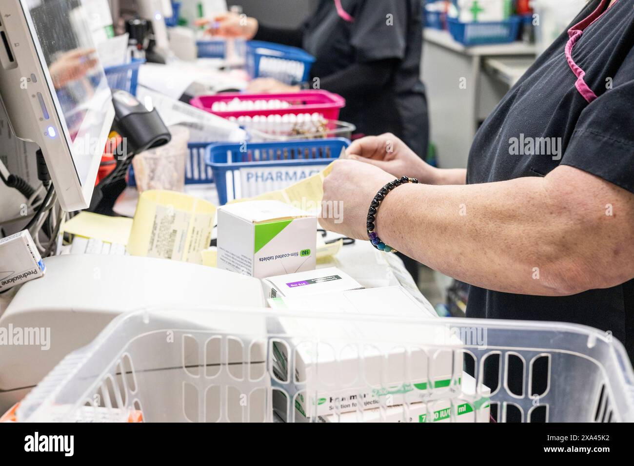 Pharmacist organizing medication boxes beside a computer in a pharmacy. Stock Photo