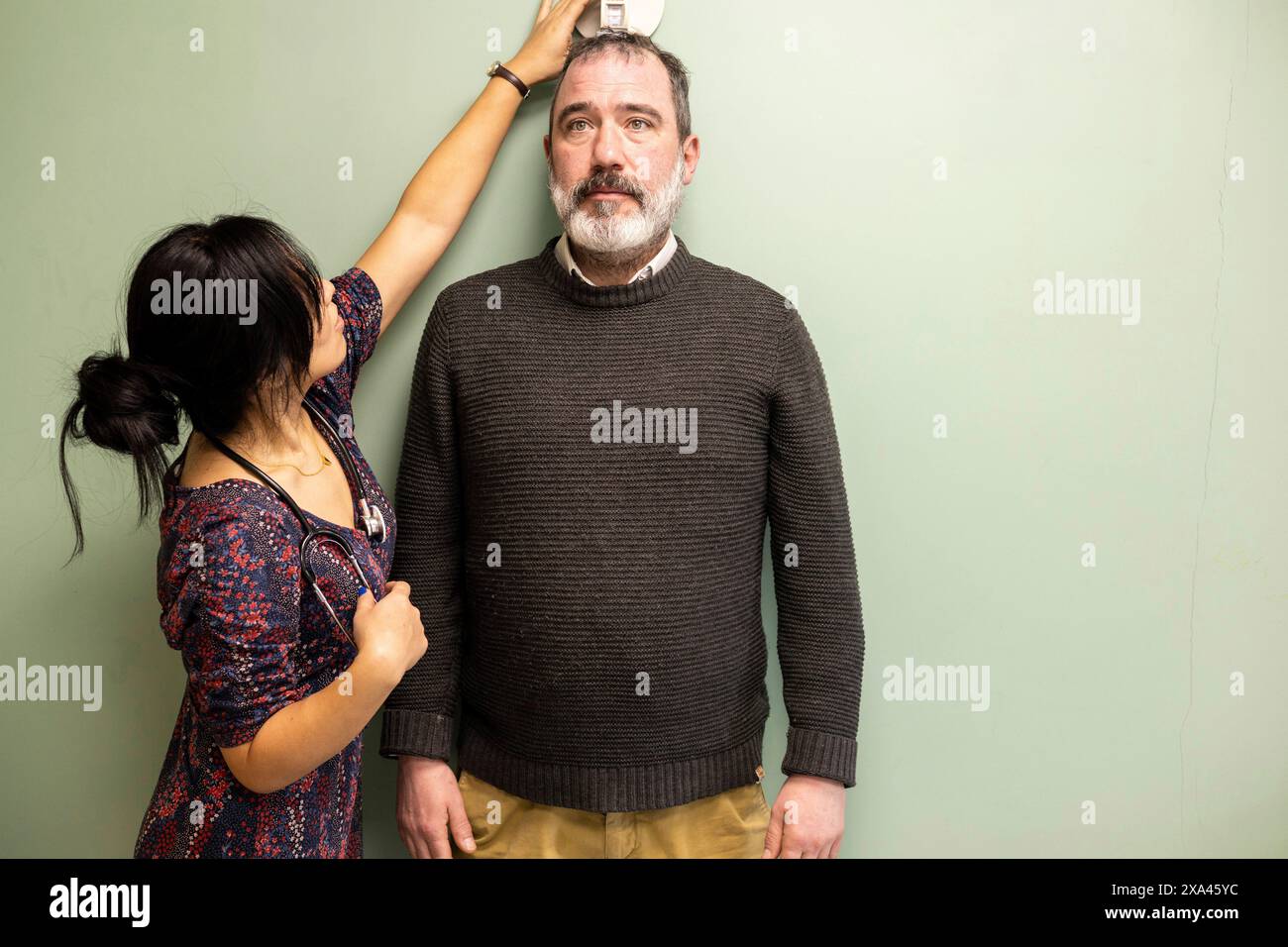 Woman measuring man's height against a wall in a medical practice Stock Photo