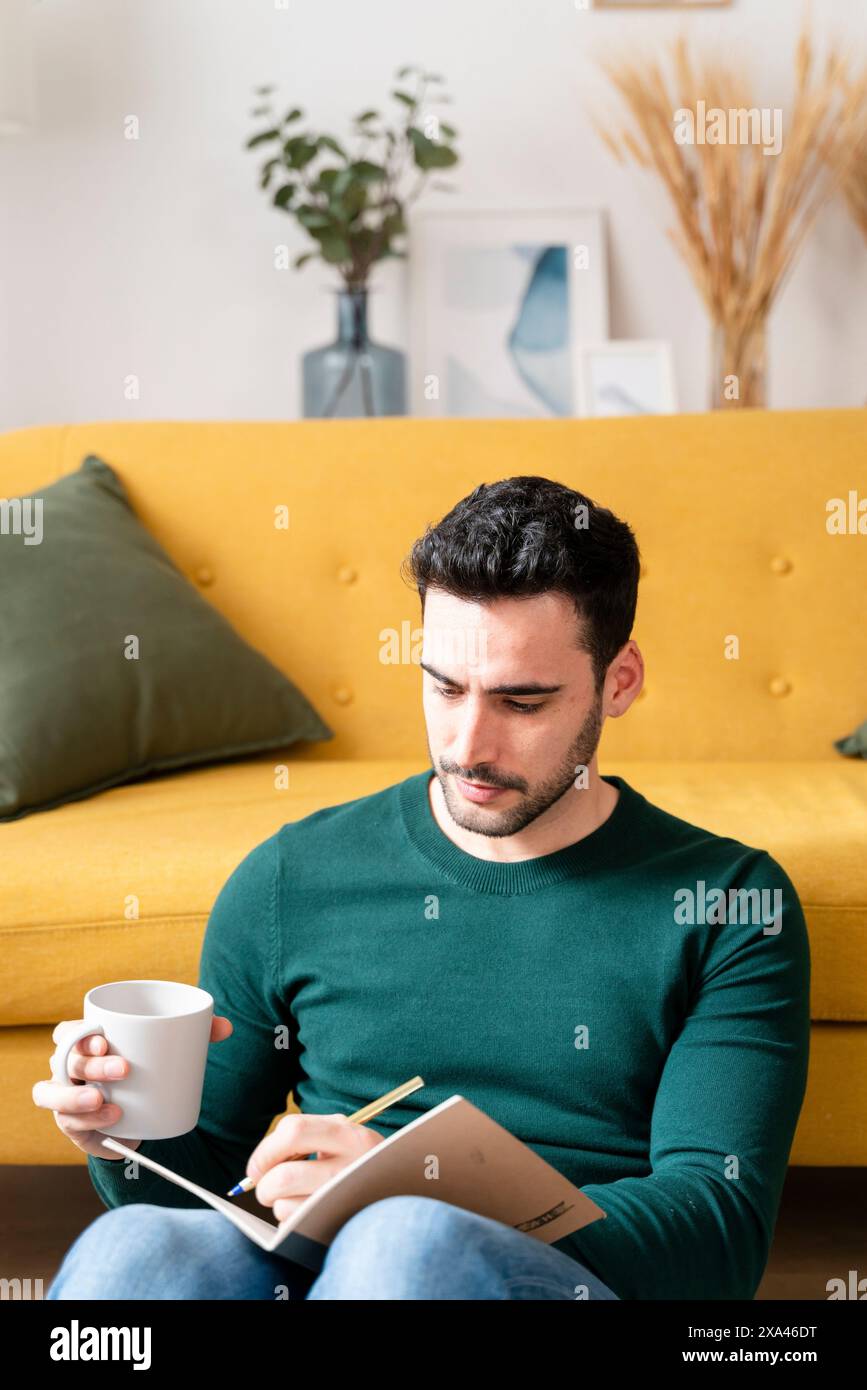 Man writing in a notebook on a yellow couch Stock Photo