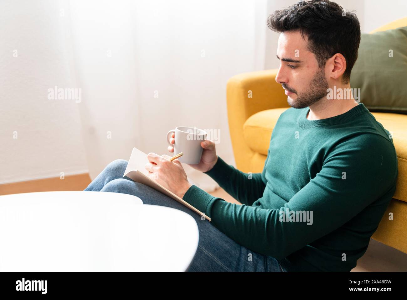 Man making notes and holding a mug on a yellow couch. Stock Photo