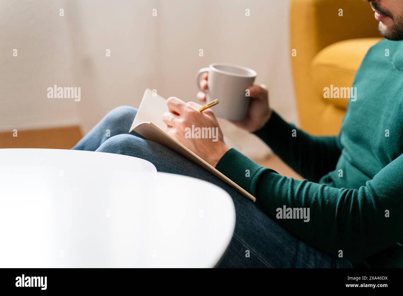 Person writing in notebook while holding a mug. Stock Photo