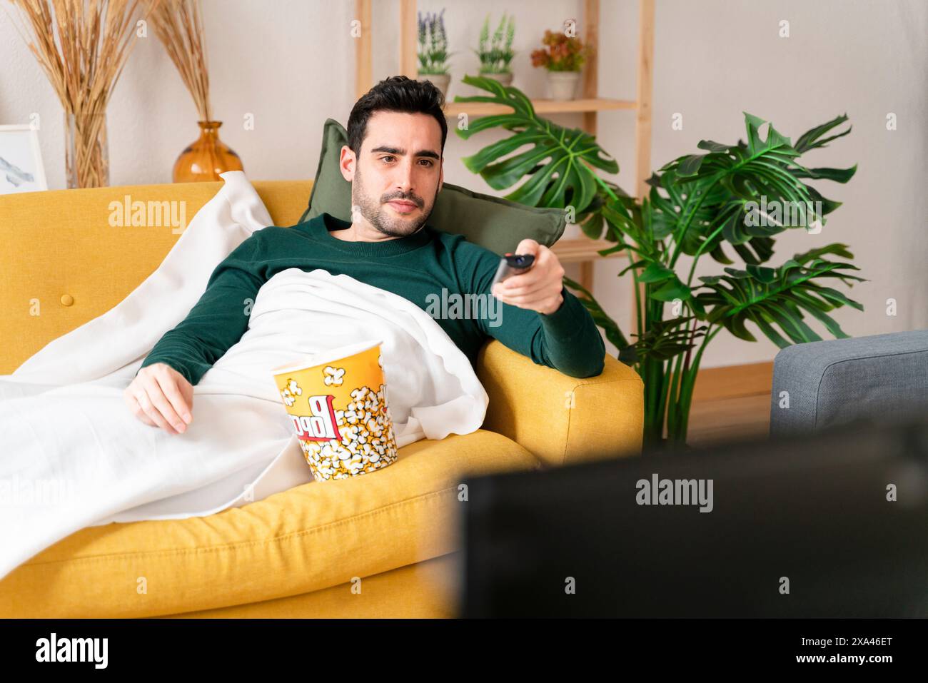 Man relaxing on couch with popcorn and remote control. Stock Photo