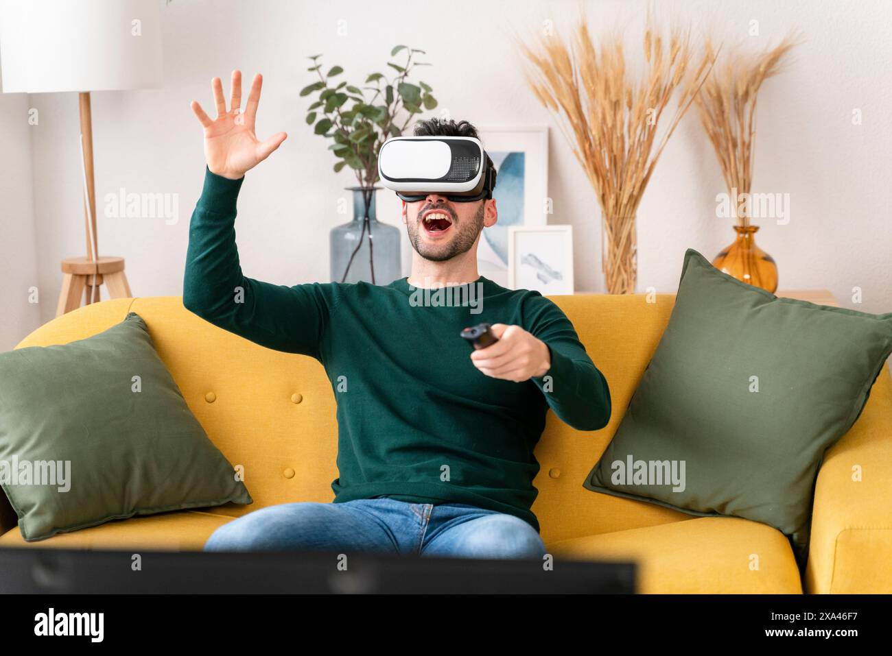 Man using VR AR headset and controller on a yellow sofa Stock Photo