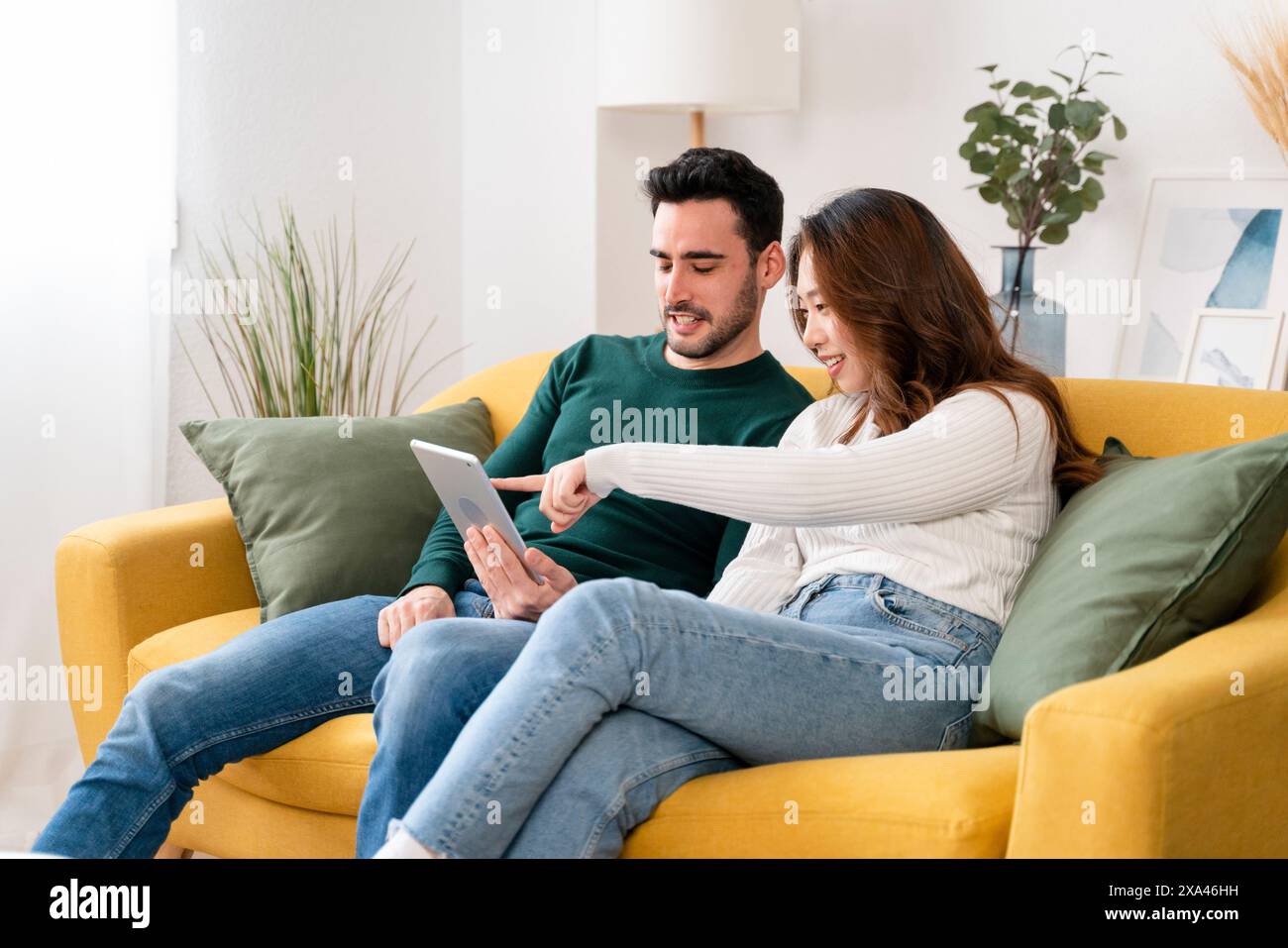 Couple sitting on a yellow sofa using a tablet Stock Photo