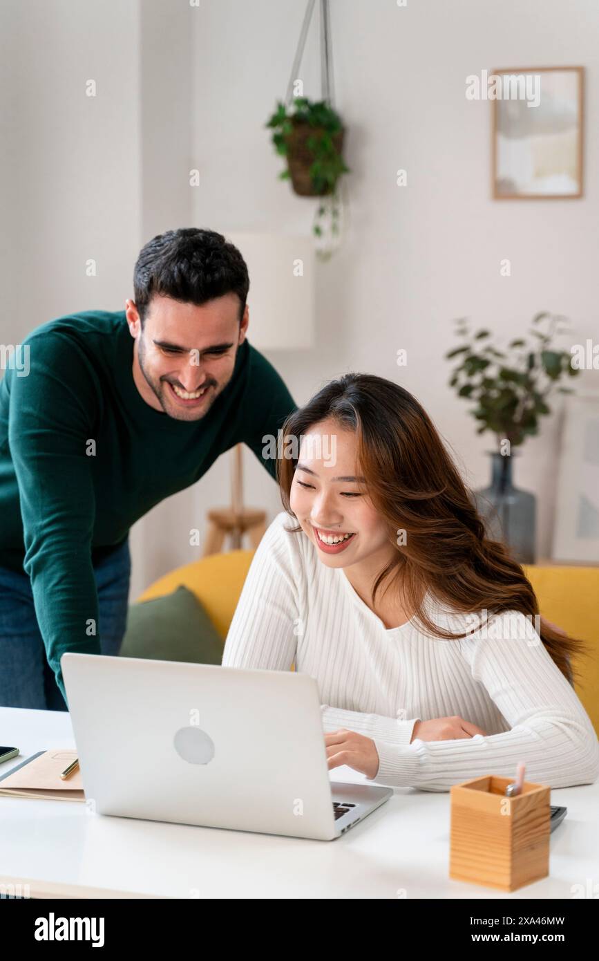 Smiling woman using laptop with man leaning over Stock Photo