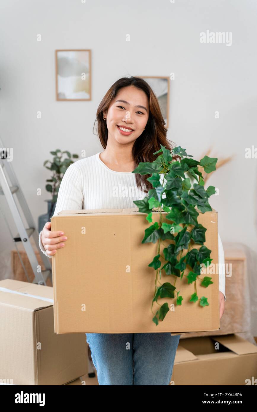 Woman smiling and holding a moving box with a plant Stock Photo