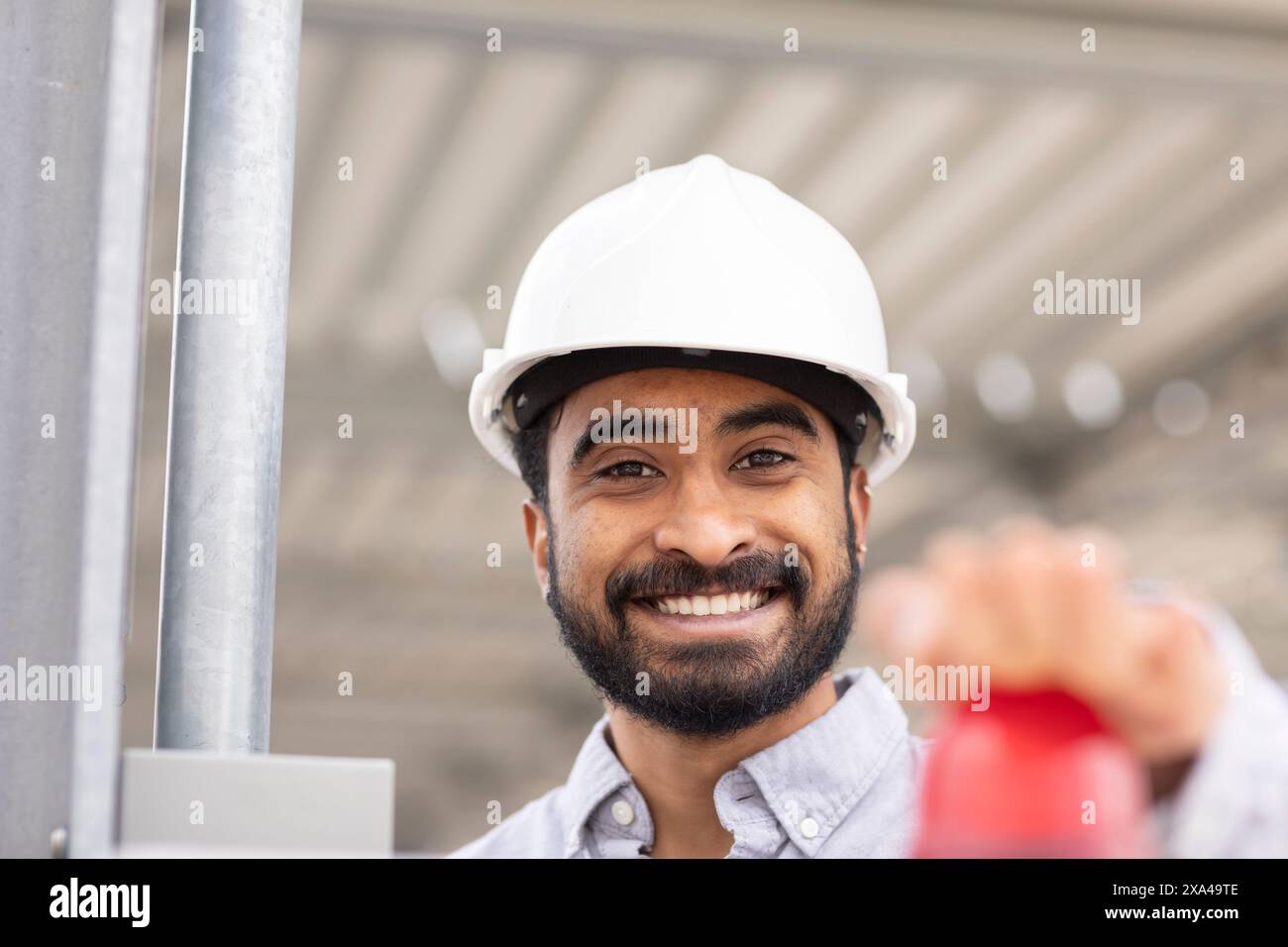 A smiling man with a beard wearing a white hard hat pressing the red button Stock Photo