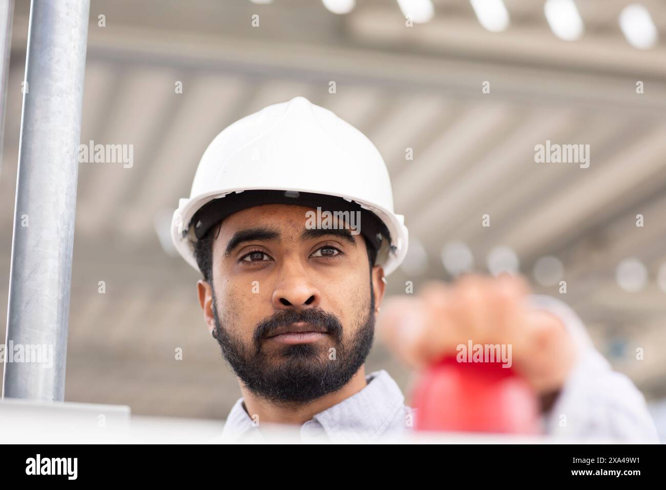 A focused man wearing a white hard hat is looking intently at something, pressing the red button Stock Photo