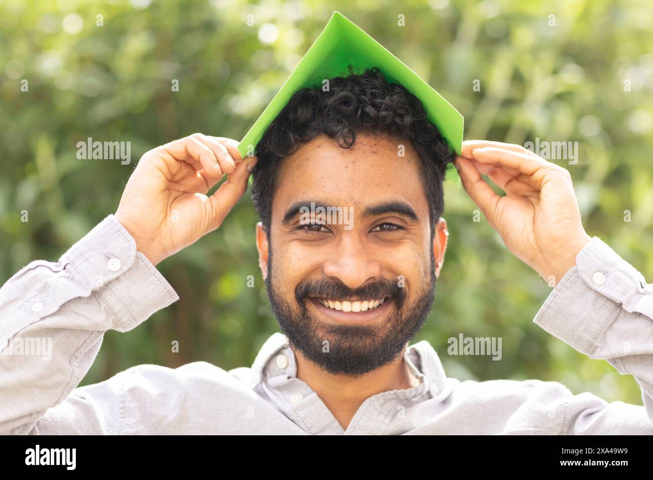 A smiling man holding a green sheet of paper over his head like a roof