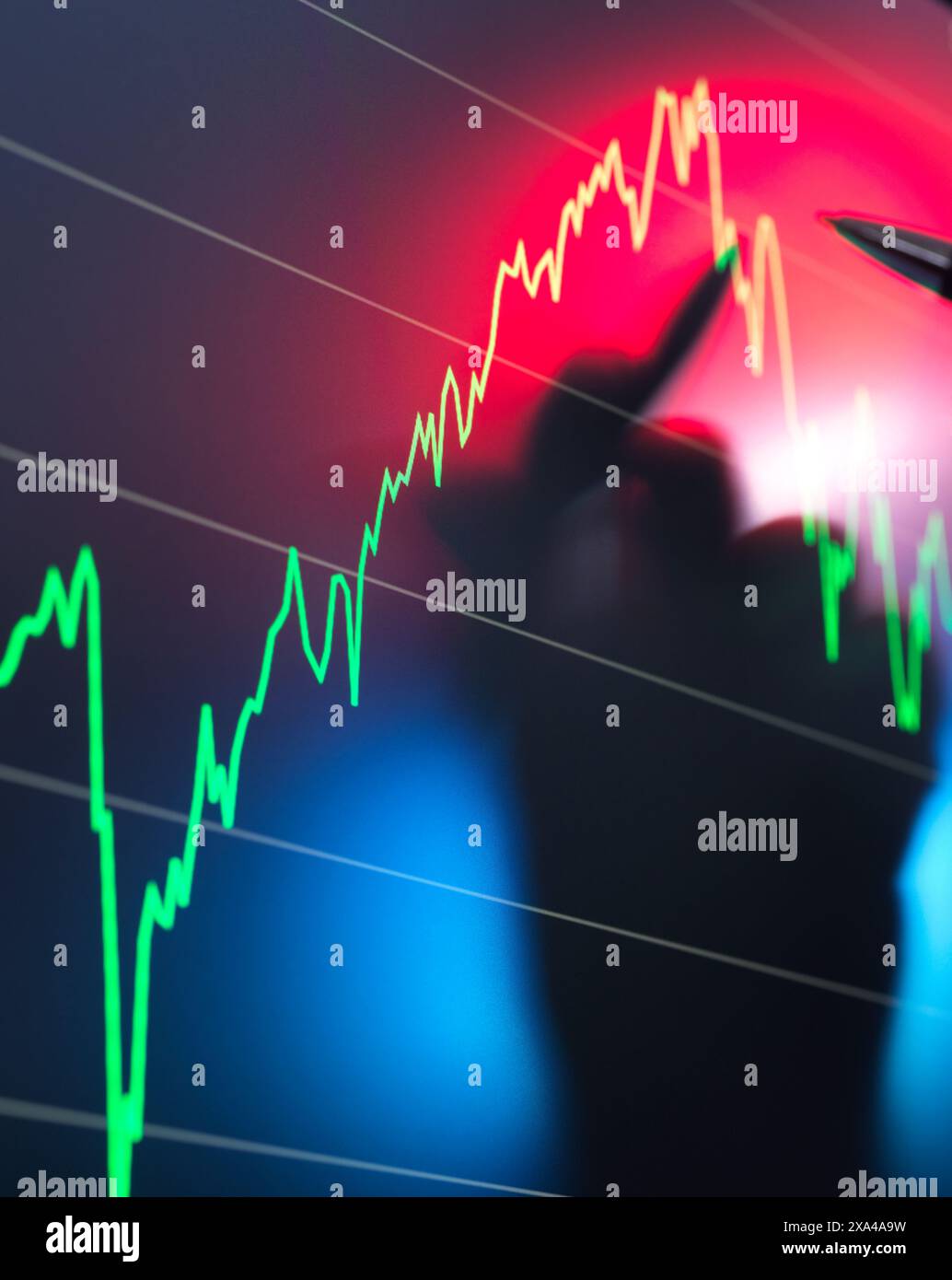A blurred silhouette of a person is seen in the foreground with a background of a stock market chart displaying a fluctuating trend line in red and green. Stock Photo