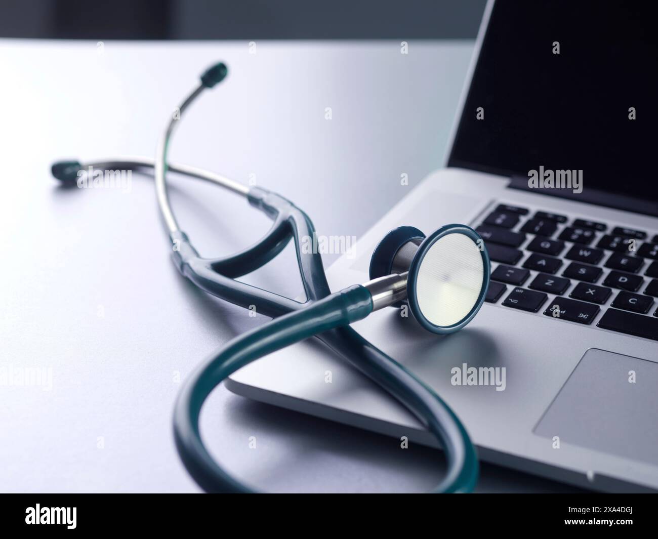 A stethoscope rests on the keyboard of a closed laptop with a silver finish, symbolizing the intersection of healthcare and technology. Stock Photo