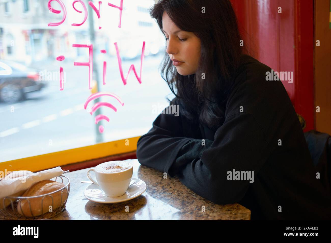 A woman sits contemplatively by a window in a cafe, with a cup of ...