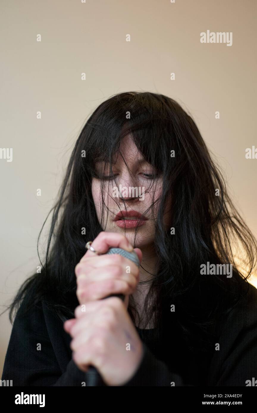 A person with tousled black hair is holding a microphone close to their face, eyes closed, giving the impression of singing passionately. Stock Photo