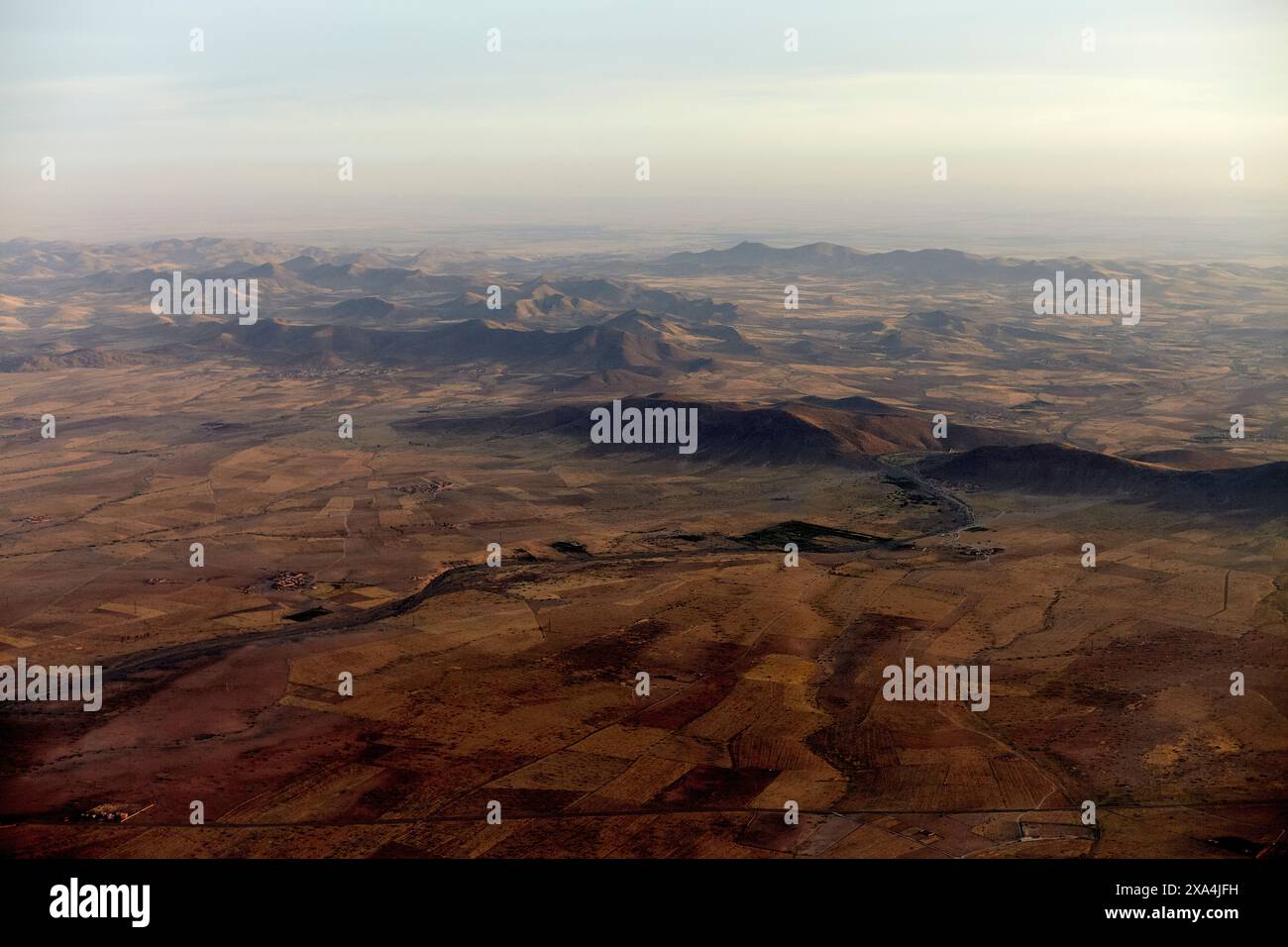 Aerial view of a vast, arid landscape under a soft glow of sunlight with mountain ranges and scattered vegetation. Stock Photo