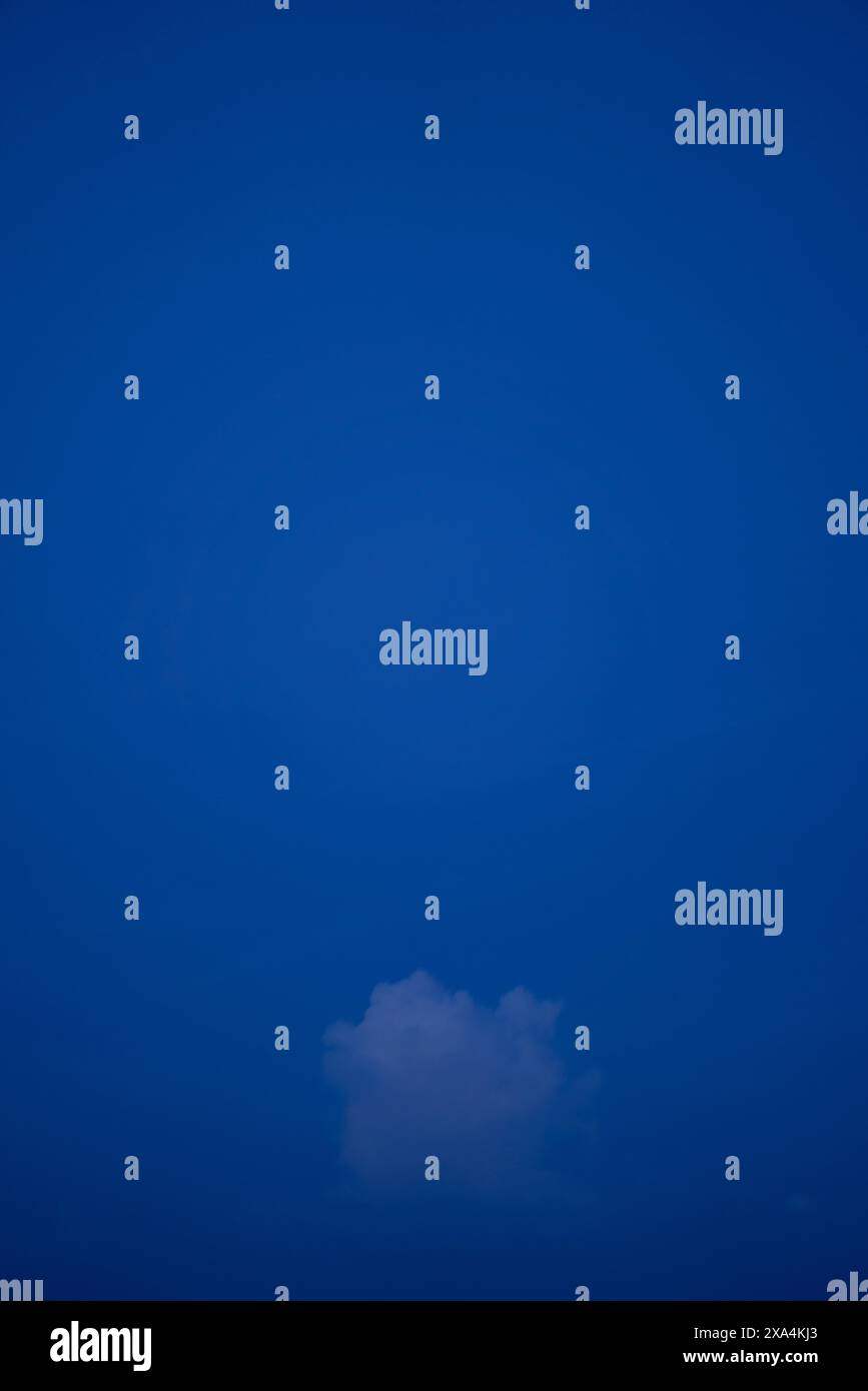 A single, small white cloud floats in a vast, deep blue sky. Stock Photo
