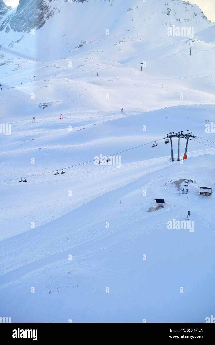 A serene, snow-covered mountain landscape with a ski lift running up the slope and skiers dotting the trails beneath a clear blue sky. Stock Photo