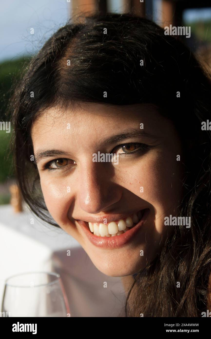 Smiling woman with dark hair enjoying a sunny day outdoors with a drink Stock Photo