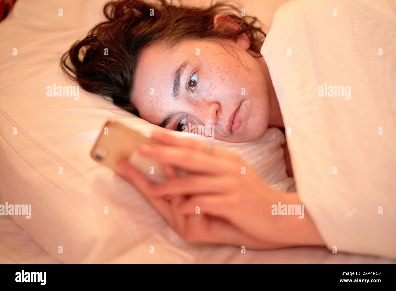 Young woman using a smartphone in bed Stock Photo