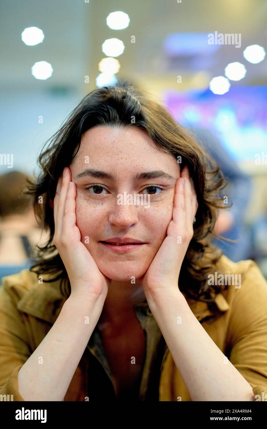 Content woman with hands on cheeks sitting indoors Stock Photo - Alamy