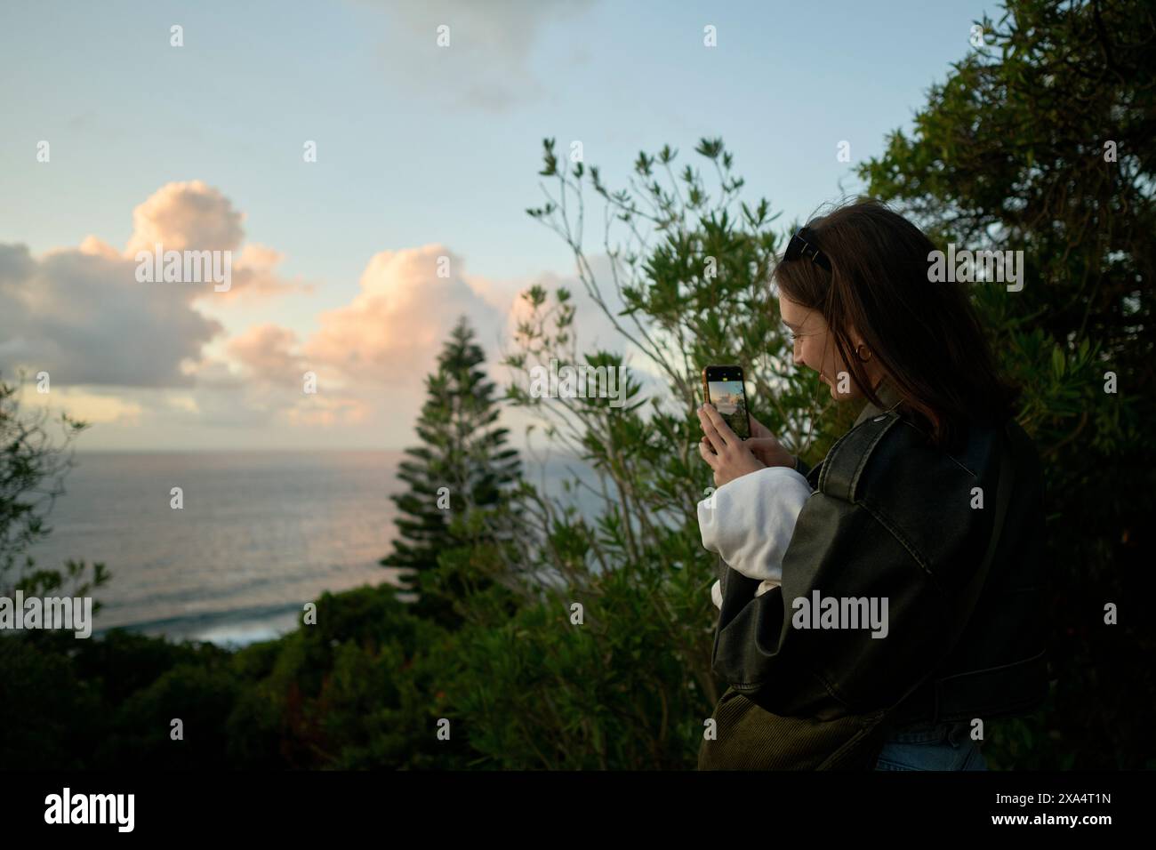 Woman using smartphone to capture the scenic view of the ocean at sunset. Stock Photo