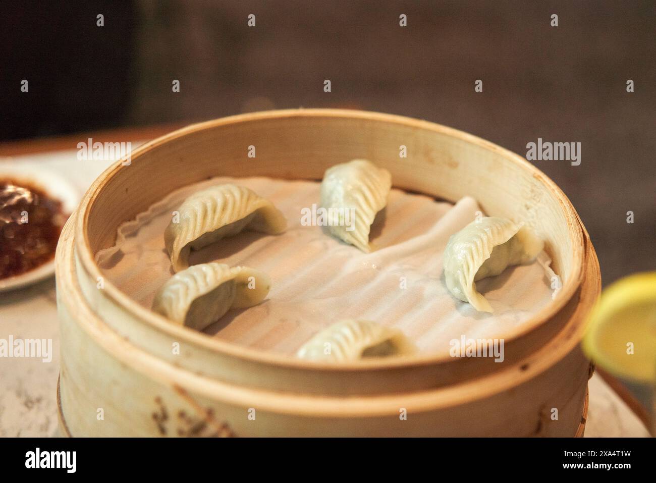 Steamed dumplings in a bamboo basket with dipping sauce on the side. Stock Photo
