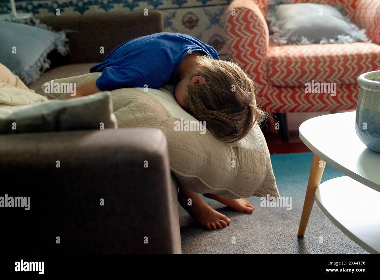 A person is taking a nap on a couch with their head resting on a cushion, in a cozy living room setting. Stock Photo
