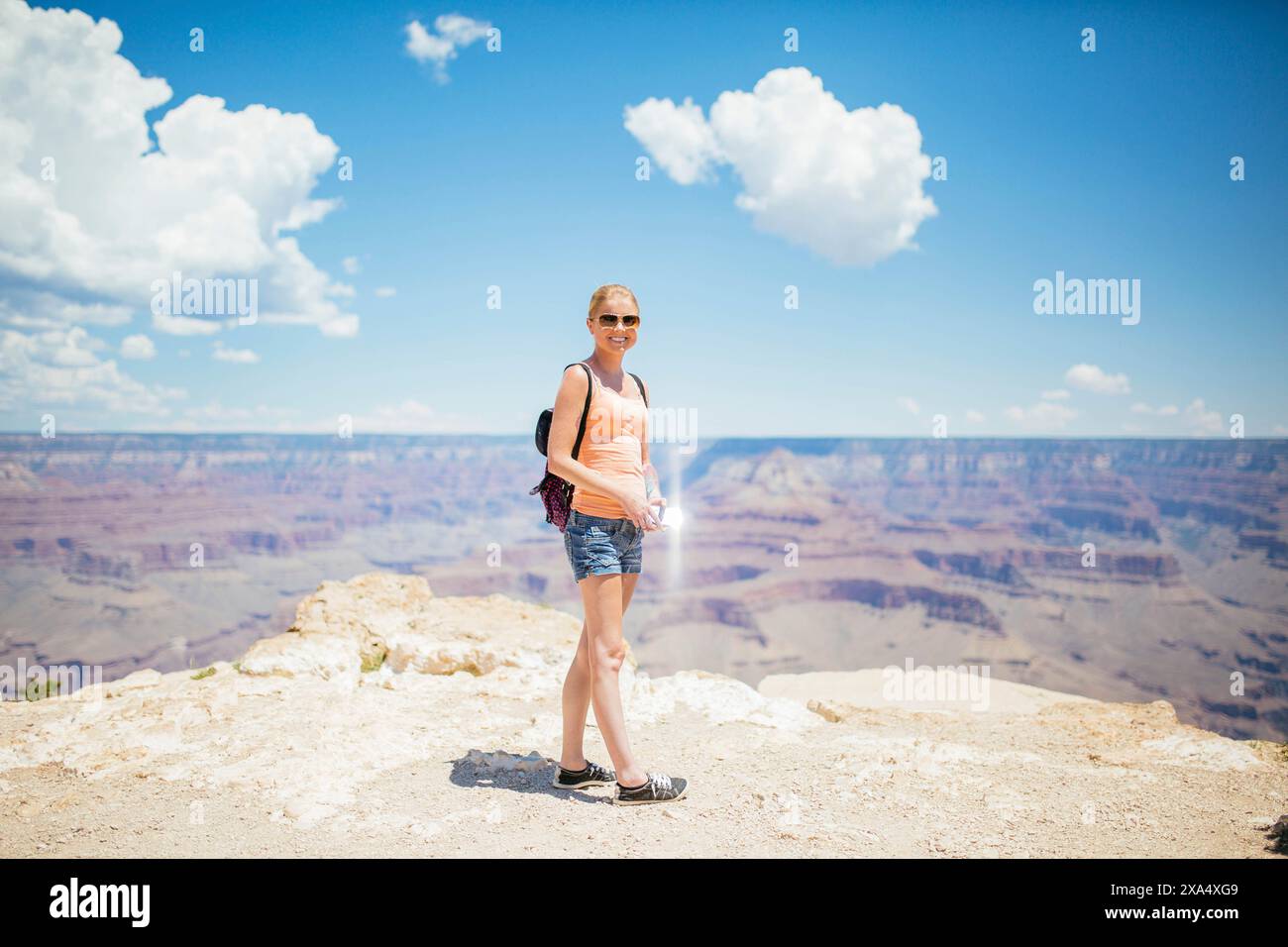 Smiling woman standing at the edge of the Grand Canyon on a sunny day ...