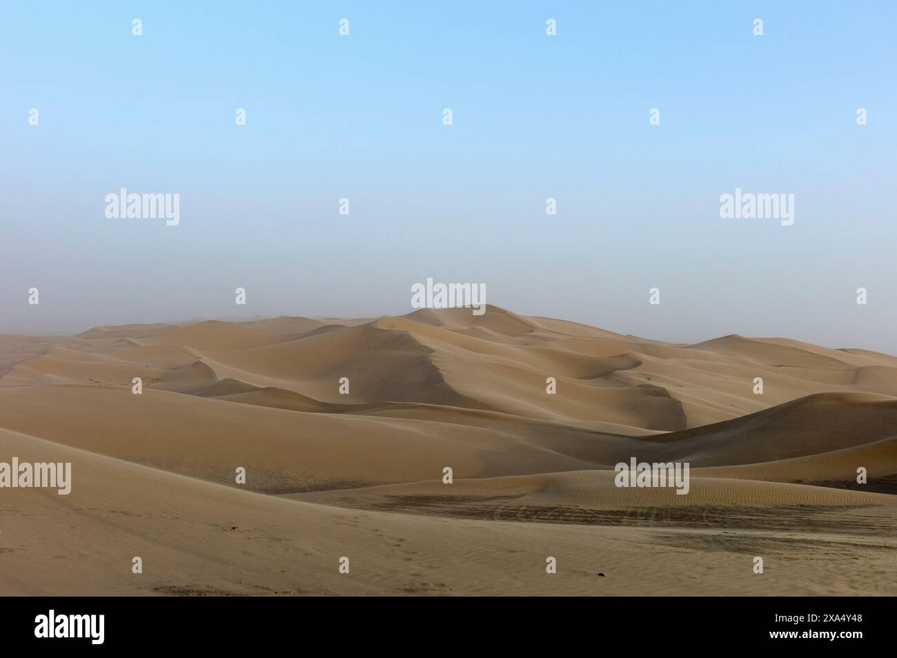 Smooth sand dunes under a hazy sky in a vast desert landscape. Stock Photo