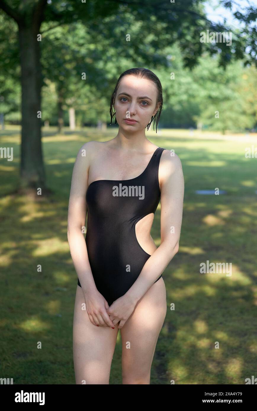 Woman in a black swimsuit standing confidently in a sunlit park. Stock Photo