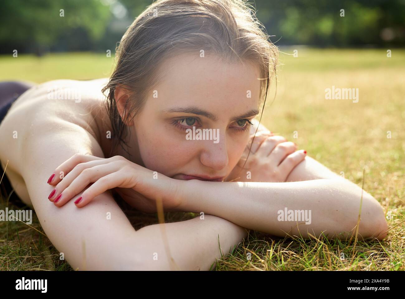 Woman relaxing on the grass with a thoughtful expression. Stock Photo