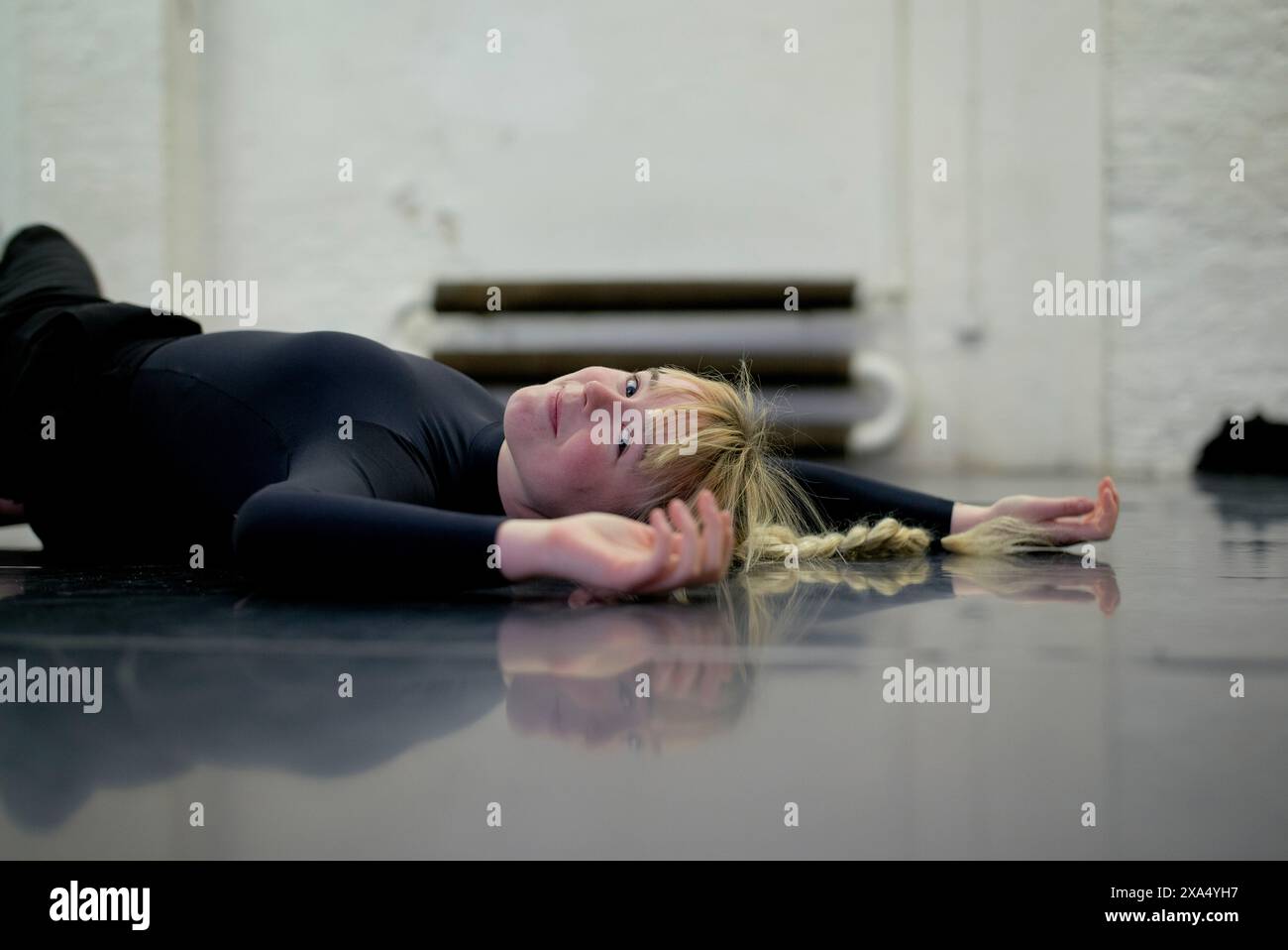 Woman in black attire resting on a shiny floor with arms outstretched Stock Photo