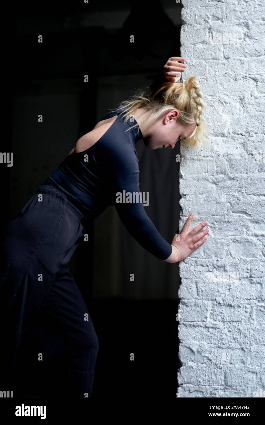 Blonde woman leaning against a white wall with a thoughtful expression. Stock Photo