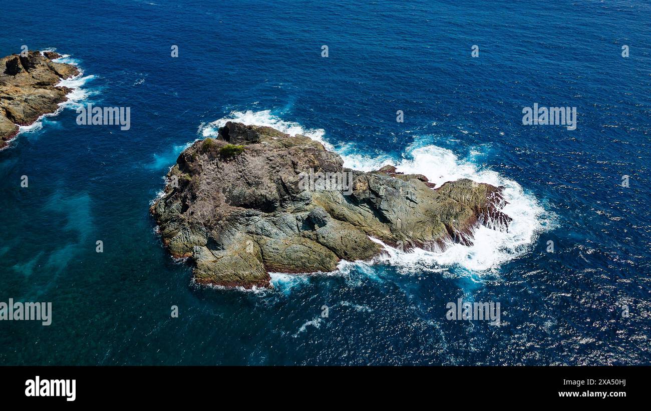 Off Shore Rocks A jagged offshore rock surrounded by waves in a deep, blue tropical ...
