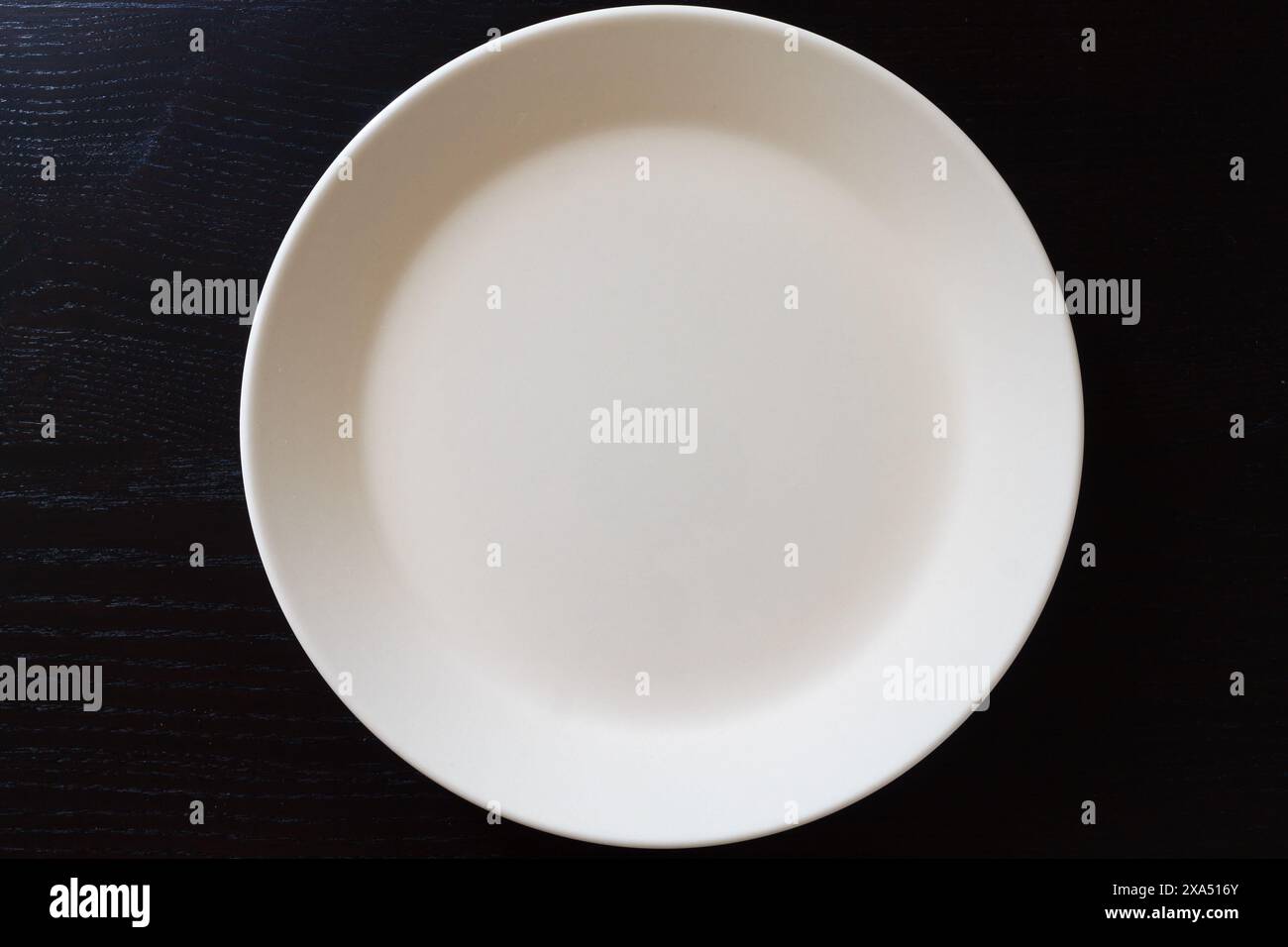 Empty white plate on black wooden table. Kitchen tools close up Stock Photo