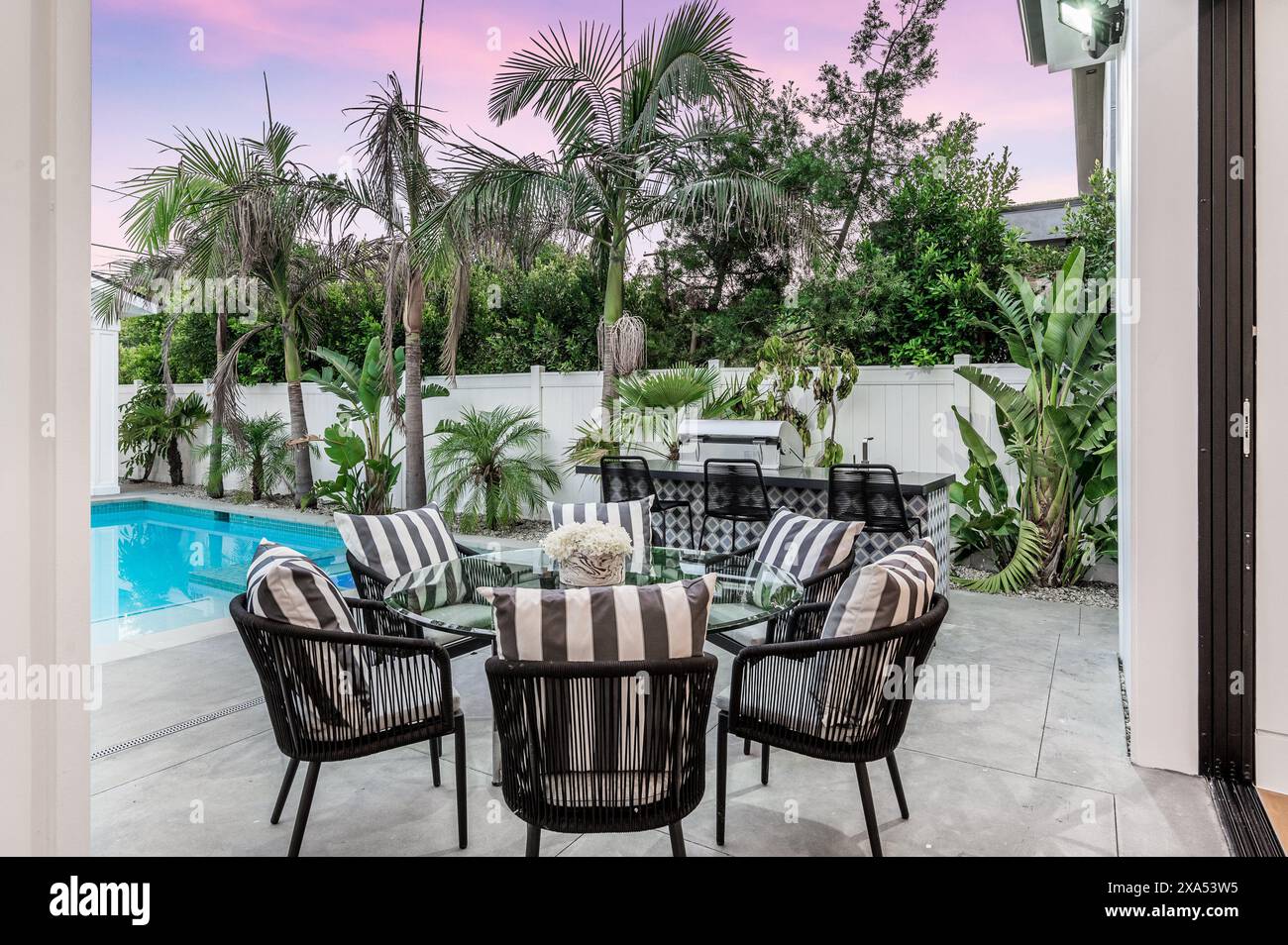 A poolside setting with a palm tree, table, and chairs in a backyard Stock Photo Alamy